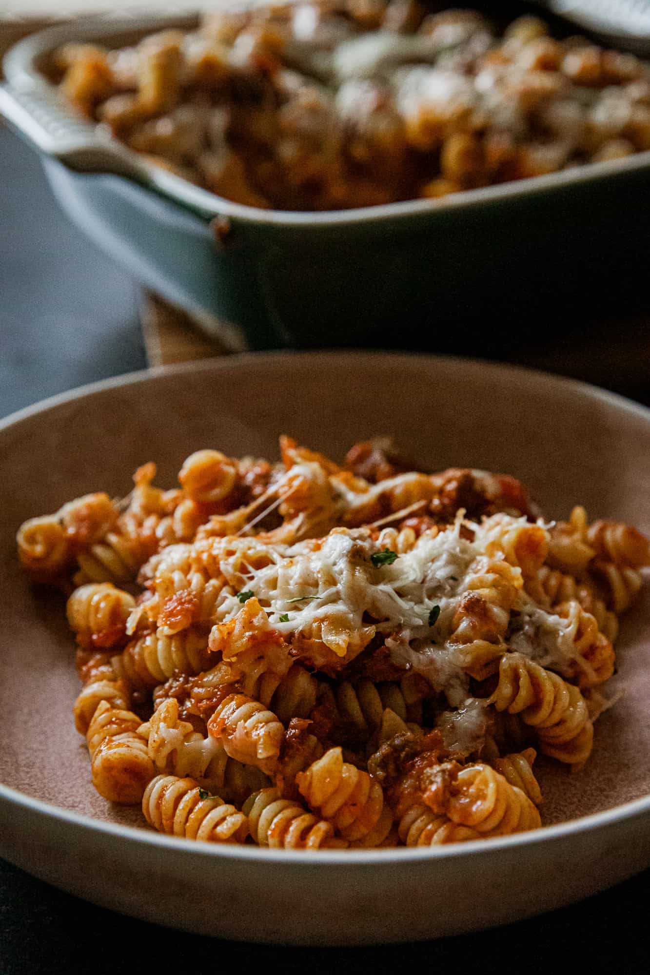 Delicious cheesy rotini pasta baked with savory sauce and melted cheese, served in a rustic bowl. Pe.