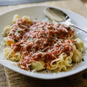 Delicious cheese tortellini topped with savory meat sauce and grated cheese, served on a white plate.