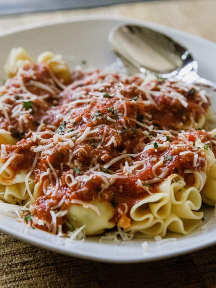 Delicious cheese tortellini topped with savory meat sauce and grated cheese, served on a white plate.