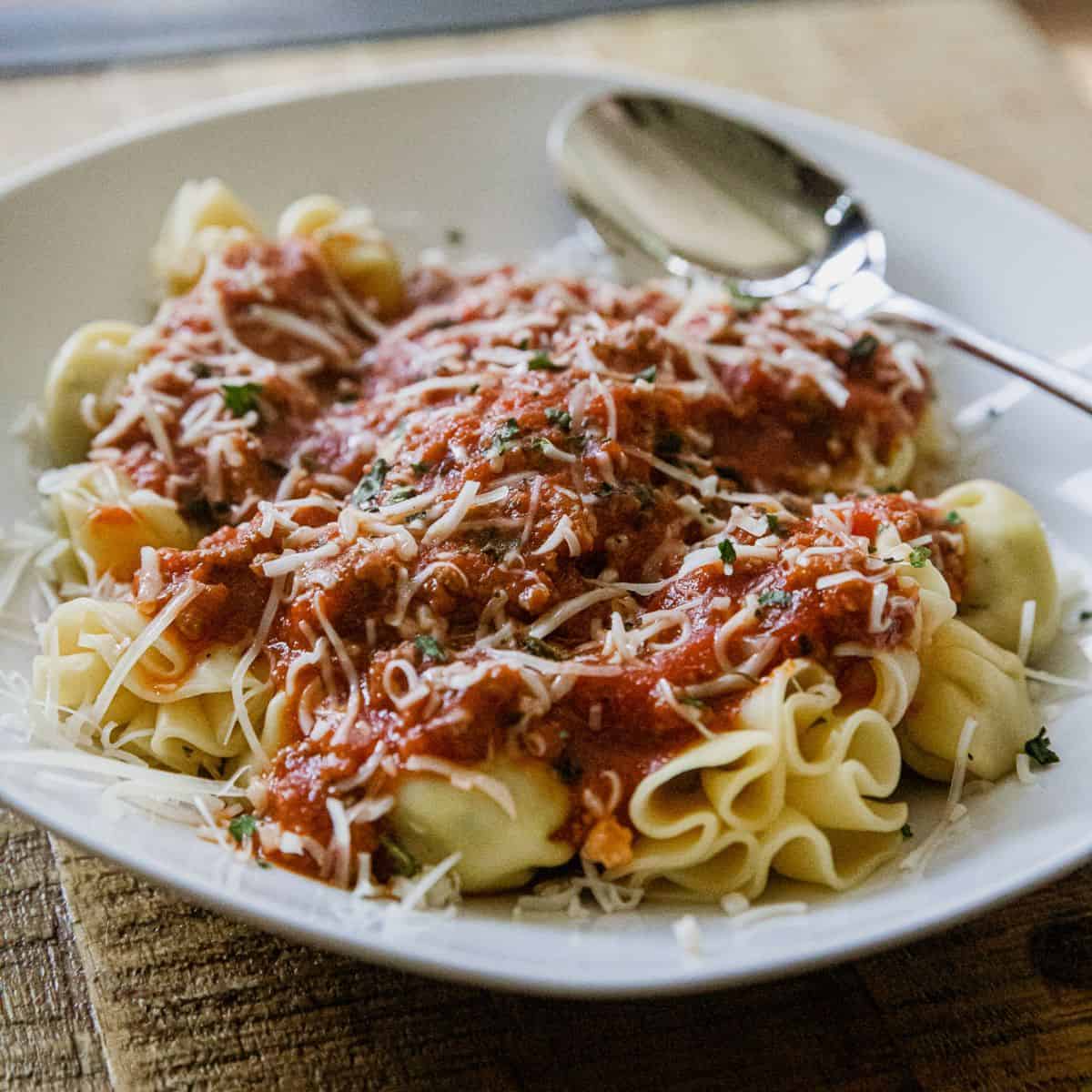 Delicious cheese tortellini topped with savory meat sauce and grated cheese, served on a white plate.