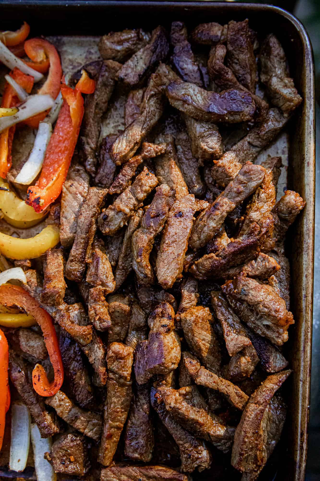 Cooked steak strips for fajitas in a skillet, with colorful peppers and onions.
