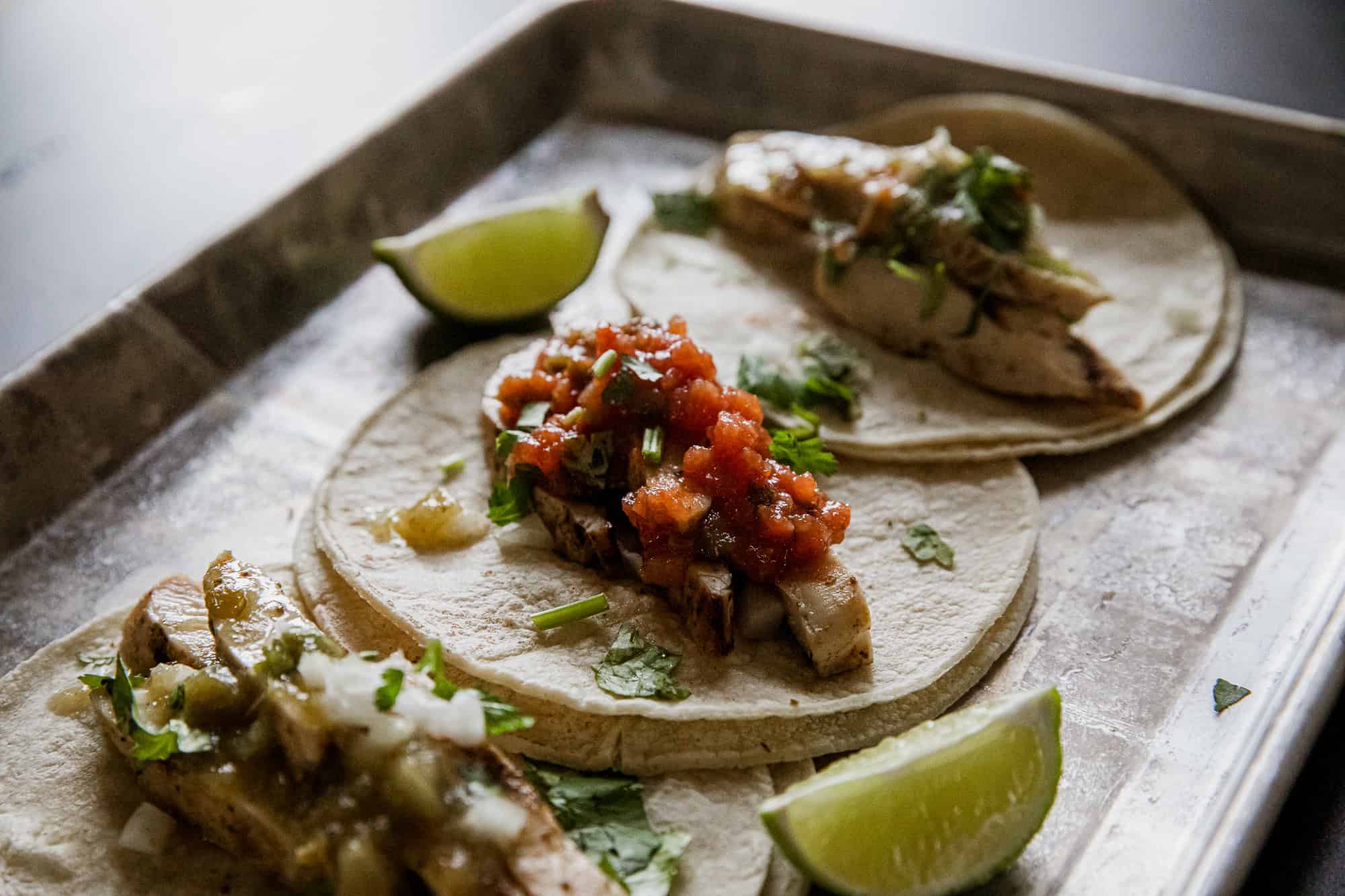 Delicious green chicken tacos with fresh toppings and lime wedges. Perfect for a flavorful Mexican-i.
