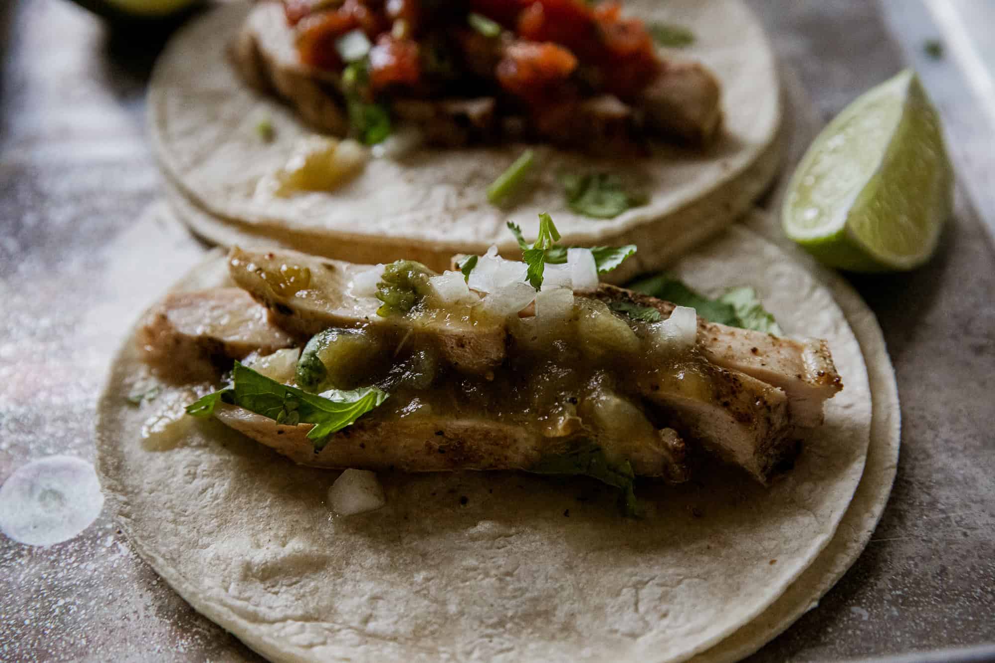 Delicious verde chicken tacos topped with fresh salsa, onions, and cilantro, served on soft corn tor.