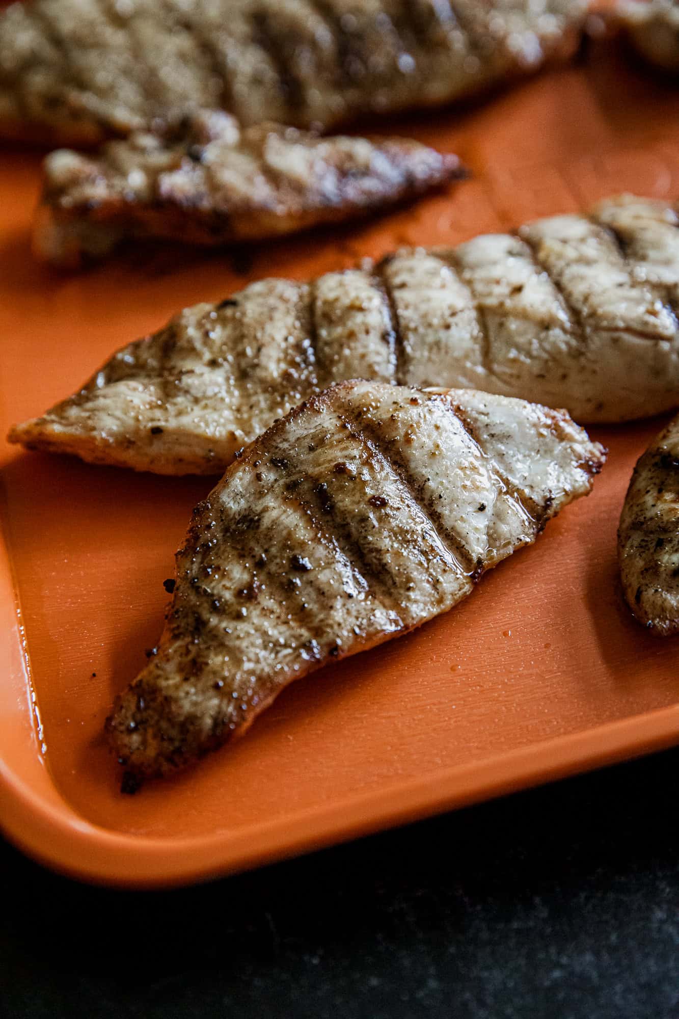 Juicy Traeger Verde grilled chicken breasts with grill marks on an orange tray.