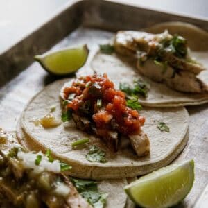 Delicious grilled chicken tacos topped with salsa, served with lime wedges.