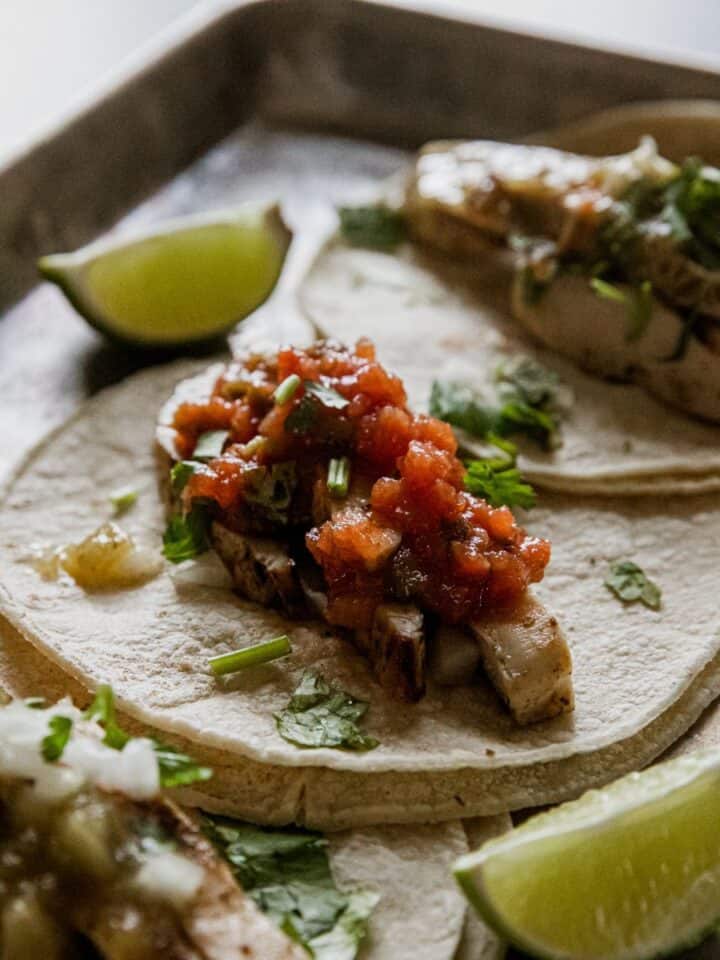 Delicious grilled chicken tacos topped with salsa, served with lime wedges.
