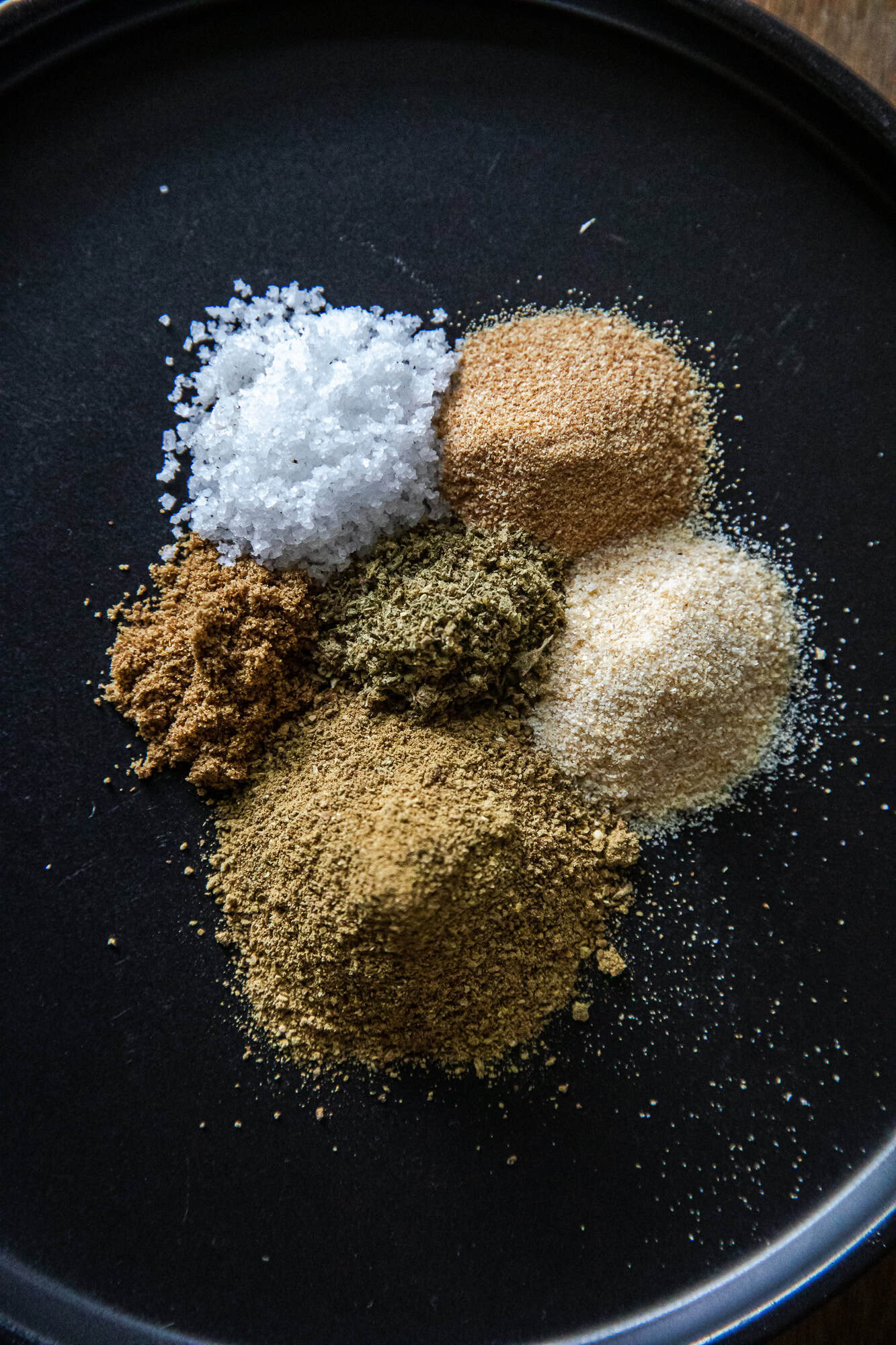 Assorted spices for Mexican Verde Rub on black background.