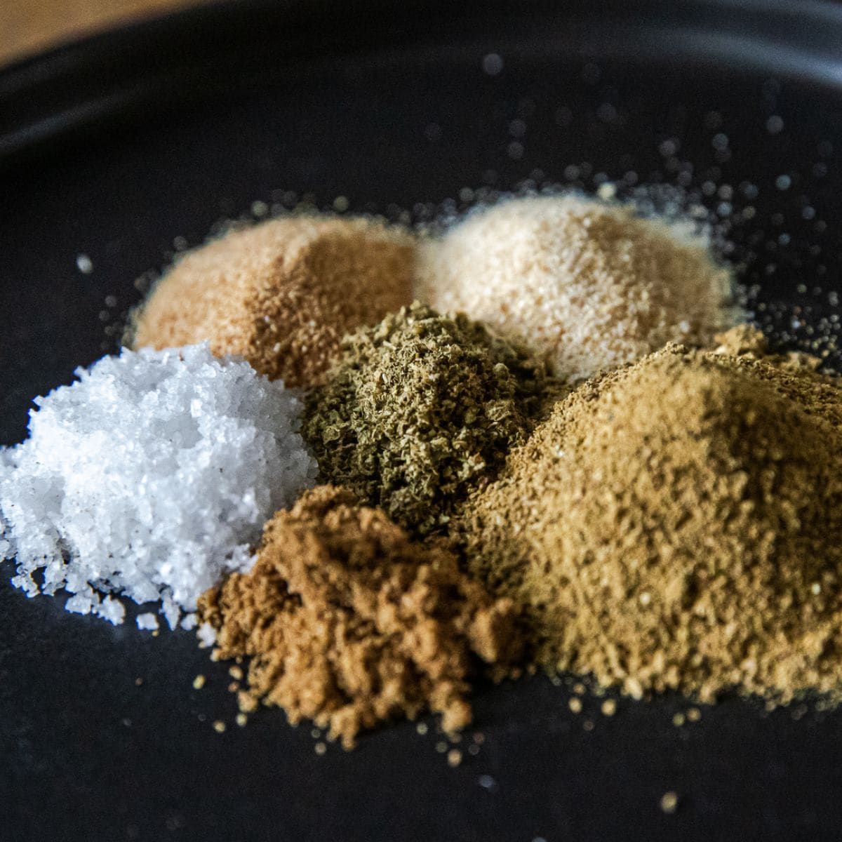 Assorted spices for Mexican Verde Rub on black background.