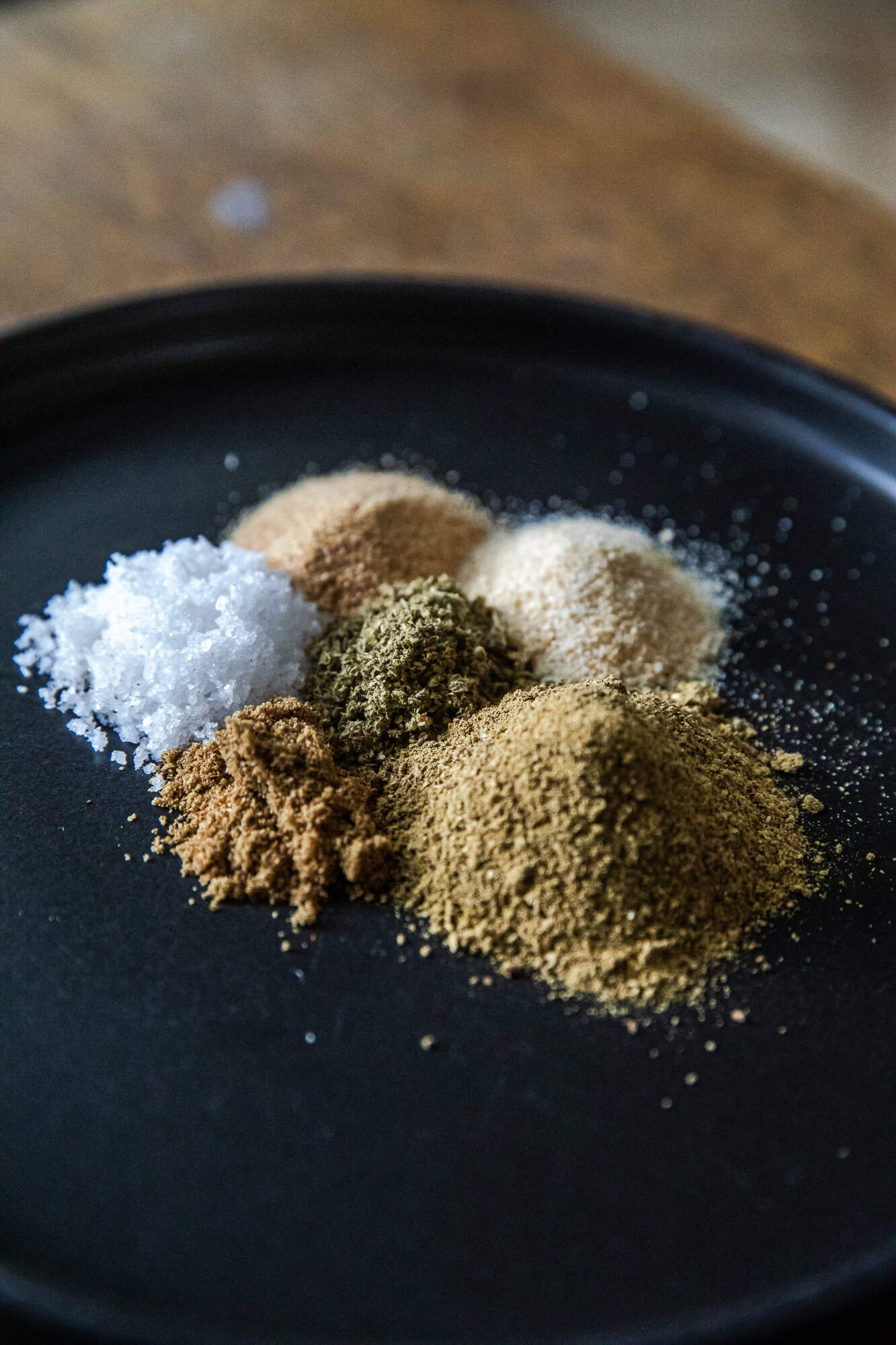 Assorted spices for Mexican Verde Rub on black plate.
