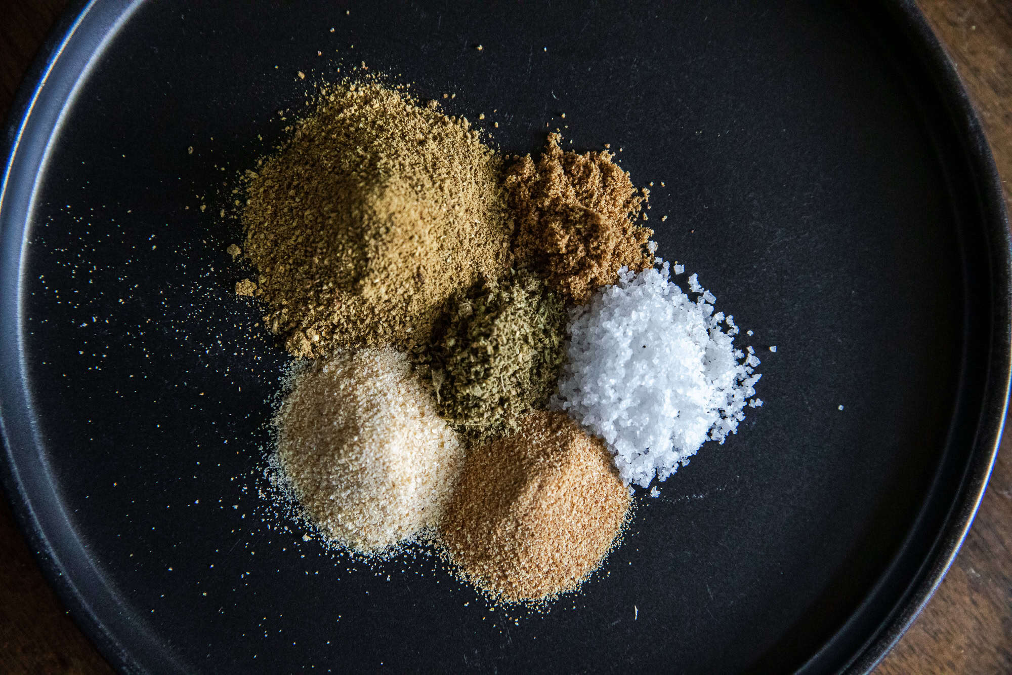 Assorted spices for Mexican Verde Rub on a black plate.