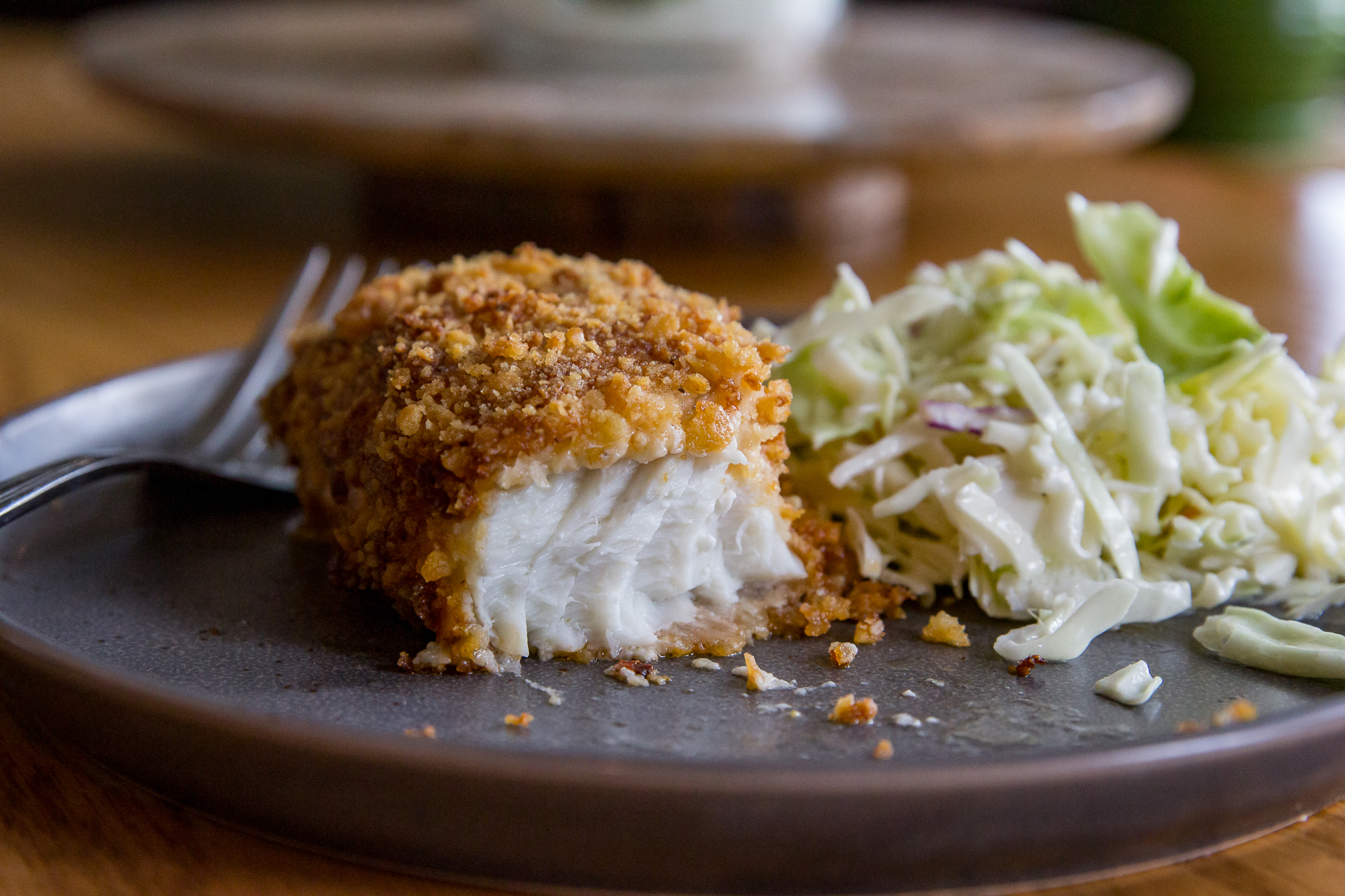 Baked crispy fish fillet served with fresh coleslaw on a dark plate.