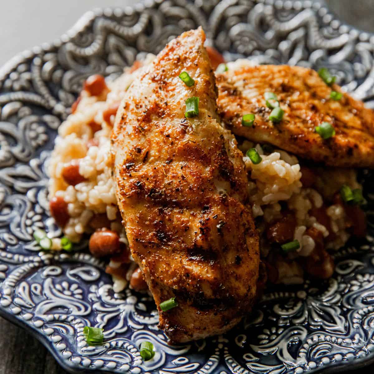 Grilled chicken thighs garnished with chopped green onions, served over rice and beans on a decorati.