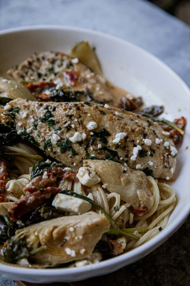 Delicious creamy chicken pasta with vegetables, herbs, and cheese in a white bowl.