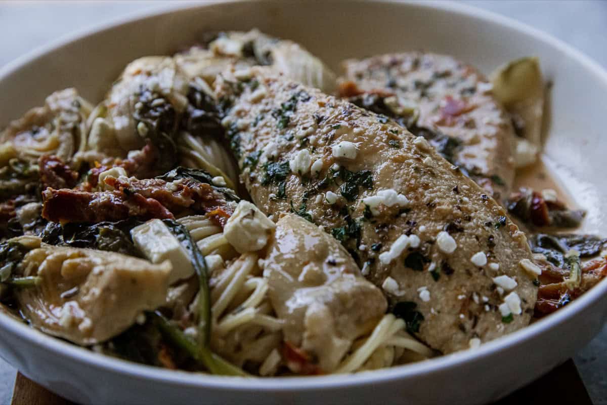 Fresh fish fillets served with pasta, vegetables, and herbs in a white bowl.