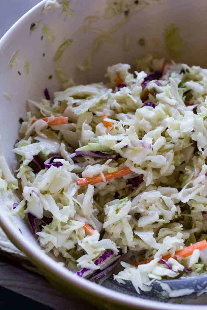 Freshly shredded coleslaw with cabbage, carrots, and purple cabbage in a white bowl.