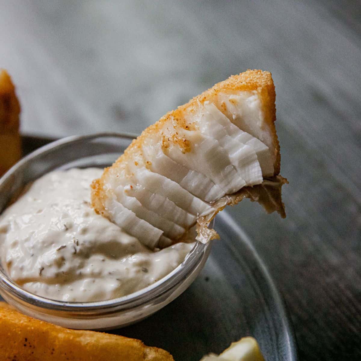 Crispy fish fillet with creamy dipping sauce served on a dark wooden table, highlighting delicious s.
