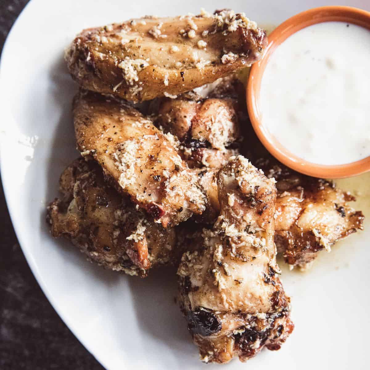 Crispy baked chicken wings served with dipping sauce on a white plate.