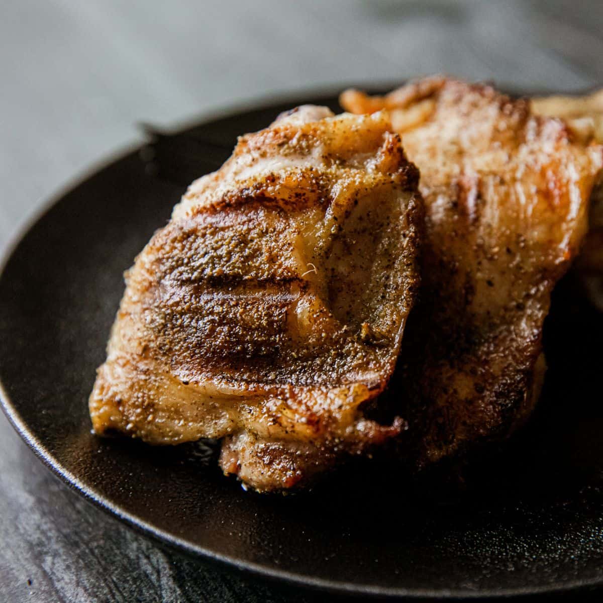 Juicy grilled pork chop served on black plate, close-up shot.