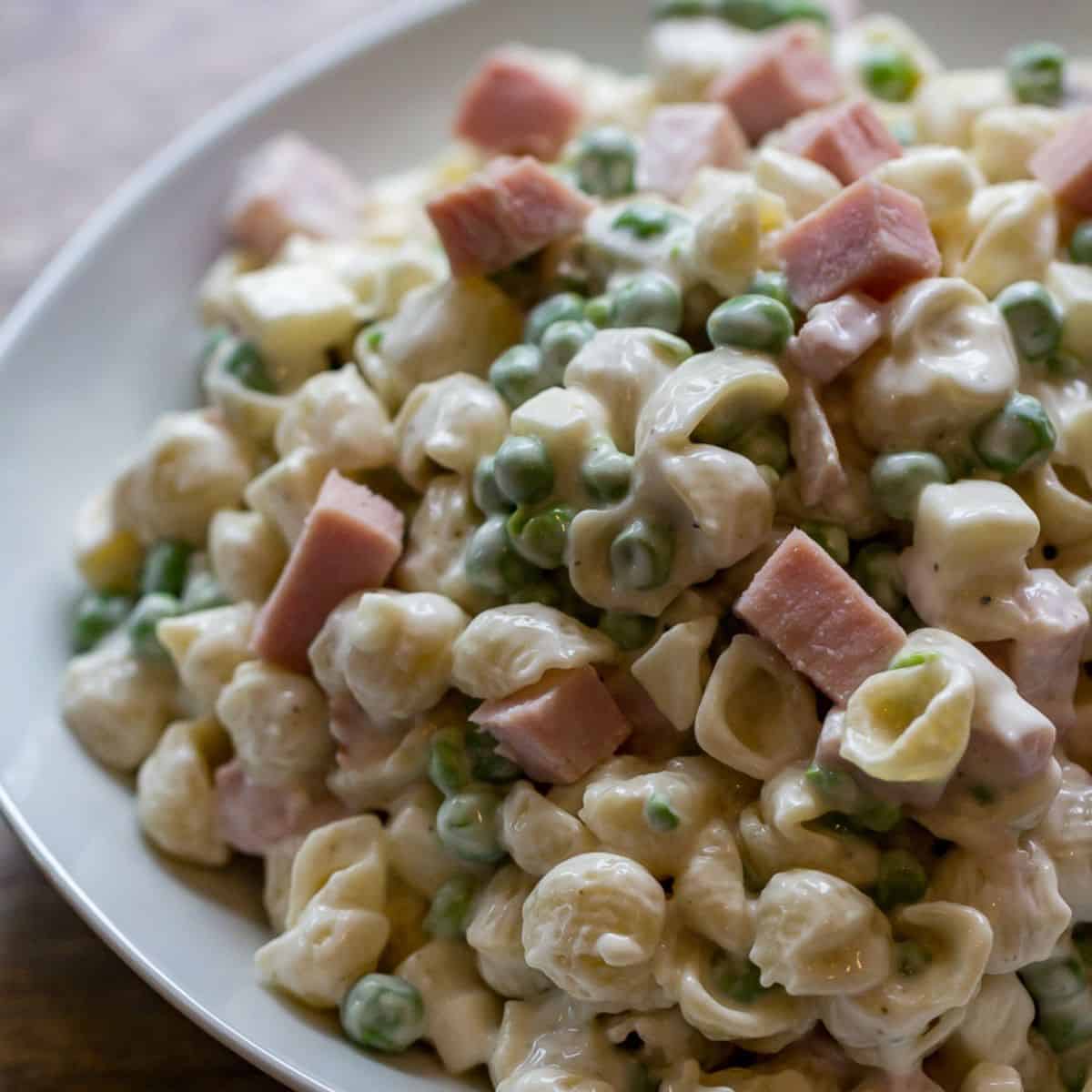 Delicious creamy ham and pea pasta salad with cheese in a white bowl.