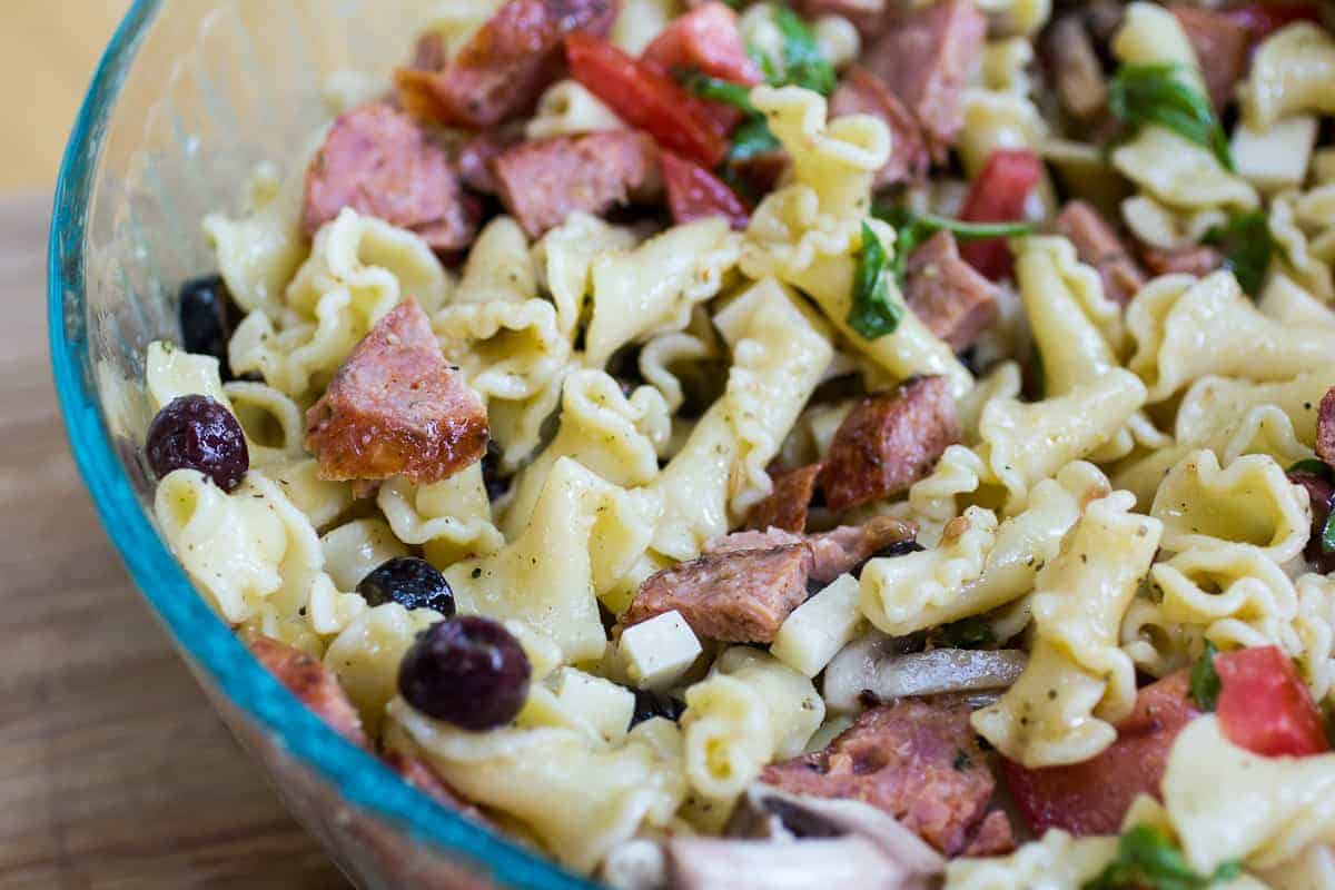 Delicious creamy pasta salad with ham, vegetables, and black olives in a glass bowl.