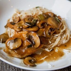 Delicious creamy mushroom chicken served with rice and gravy on a white plate.