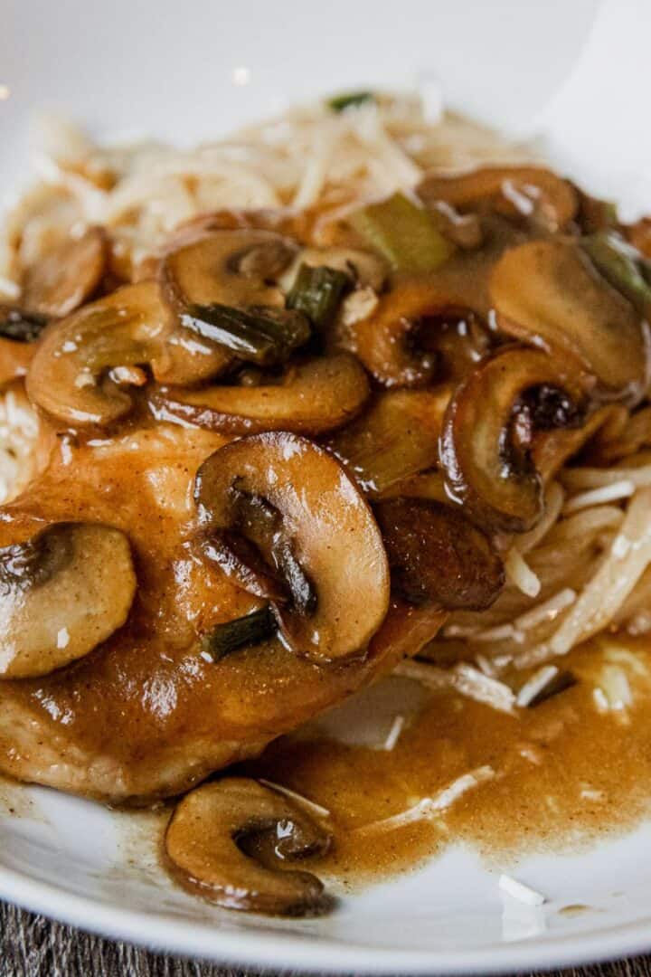 Delicious creamy mushroom chicken served with rice and gravy on a white plate.