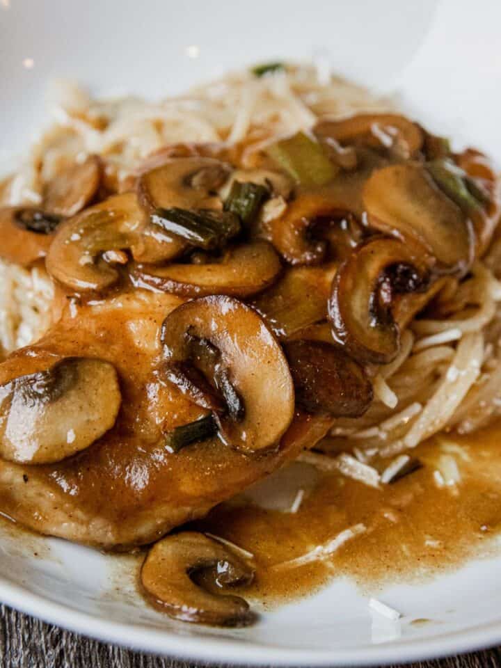 Delicious creamy mushroom chicken served with rice and gravy on a white plate.