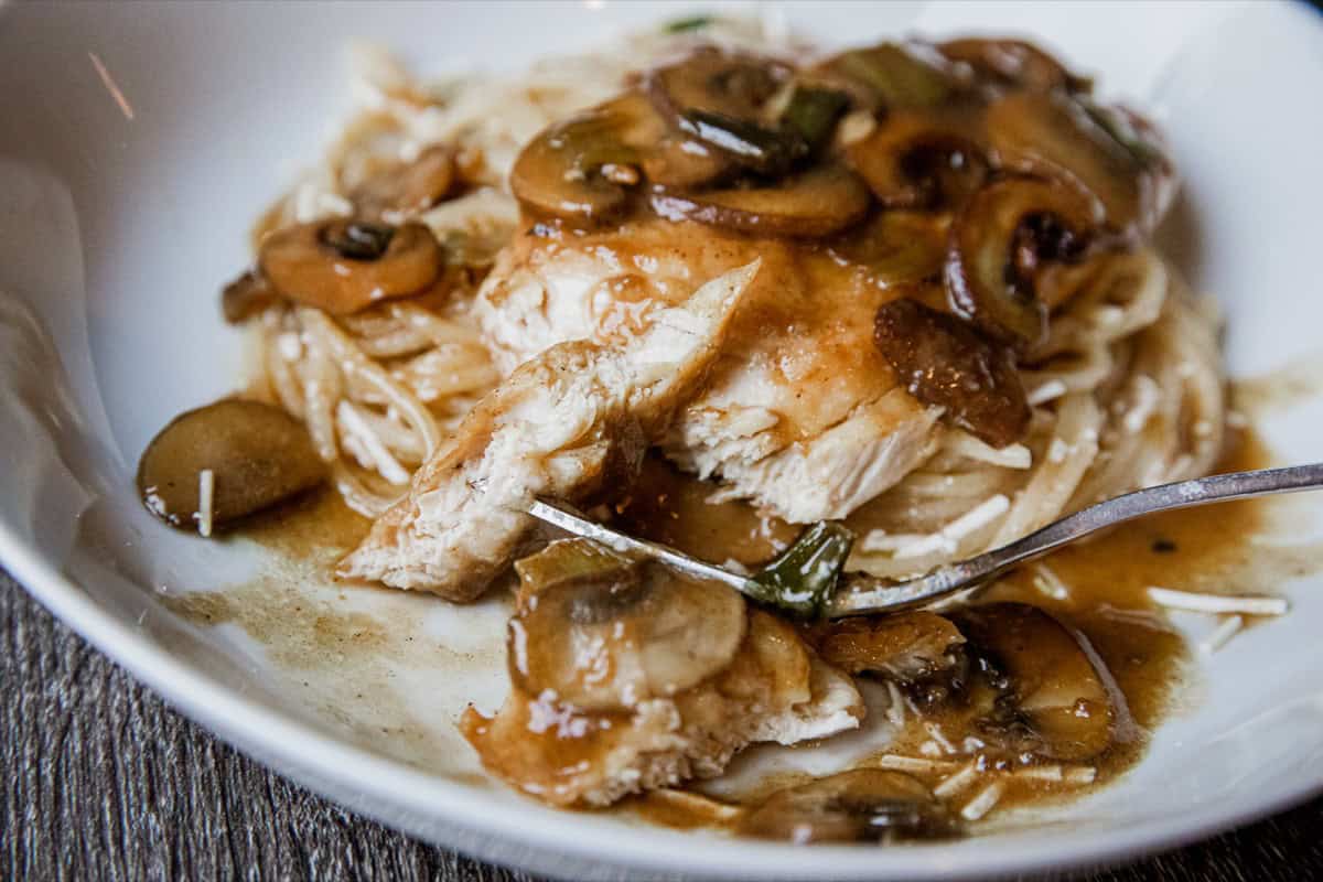 Chicken with mushroom gravy over noodles, served in a white bowl.