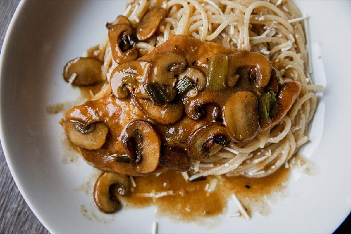 Creamy mushroom pasta with sauce, sautéed mushrooms, and vegetables on a white plate.