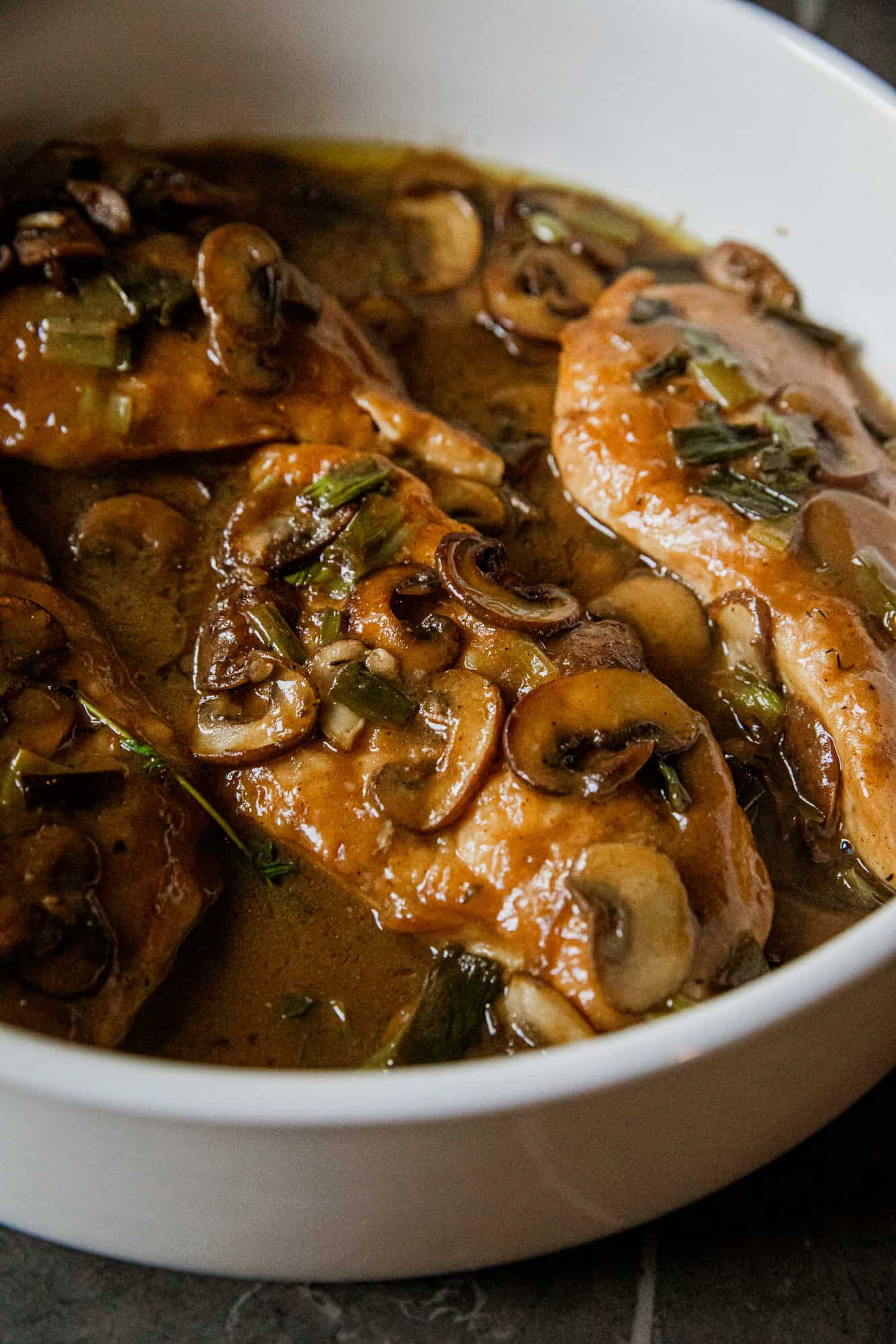 Chicken cooked with mushrooms, herbs, and savory broth in a white bowl.