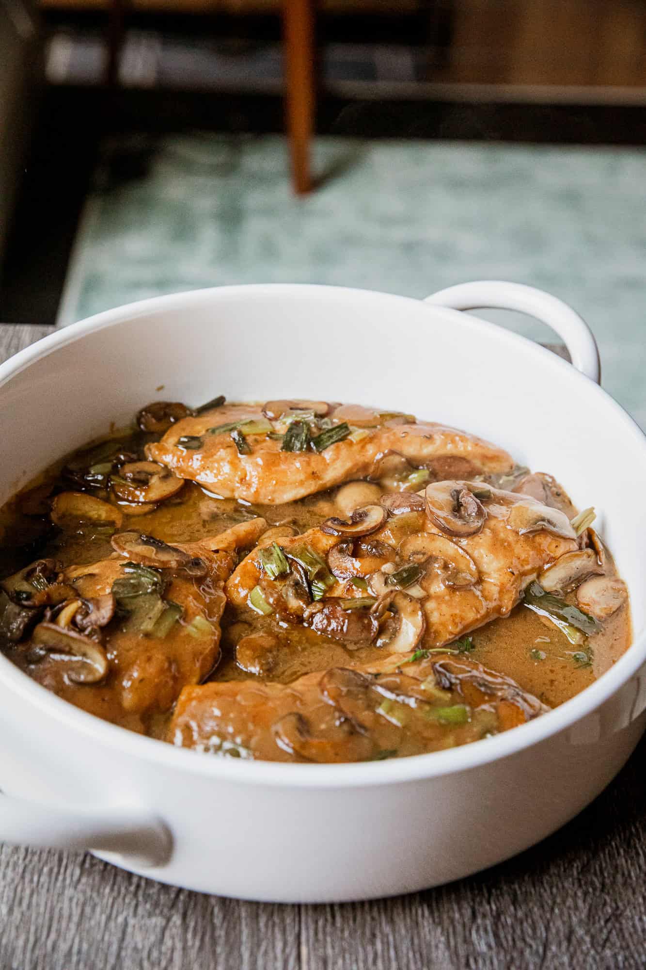 Chicken cooked with mushrooms and green onions in a savory sauce in a white ceramic dish.