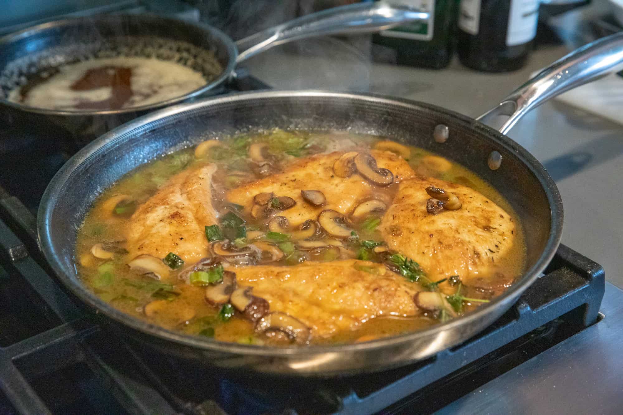 Chicken with mushroom sauce in a skillet on stovetop, garnished with herbs, cooking for a delicious.
