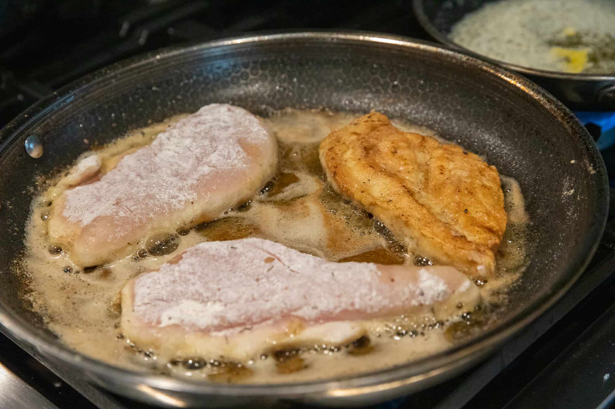 Chicken breasts cooking in a skillet with butter and seasoning.