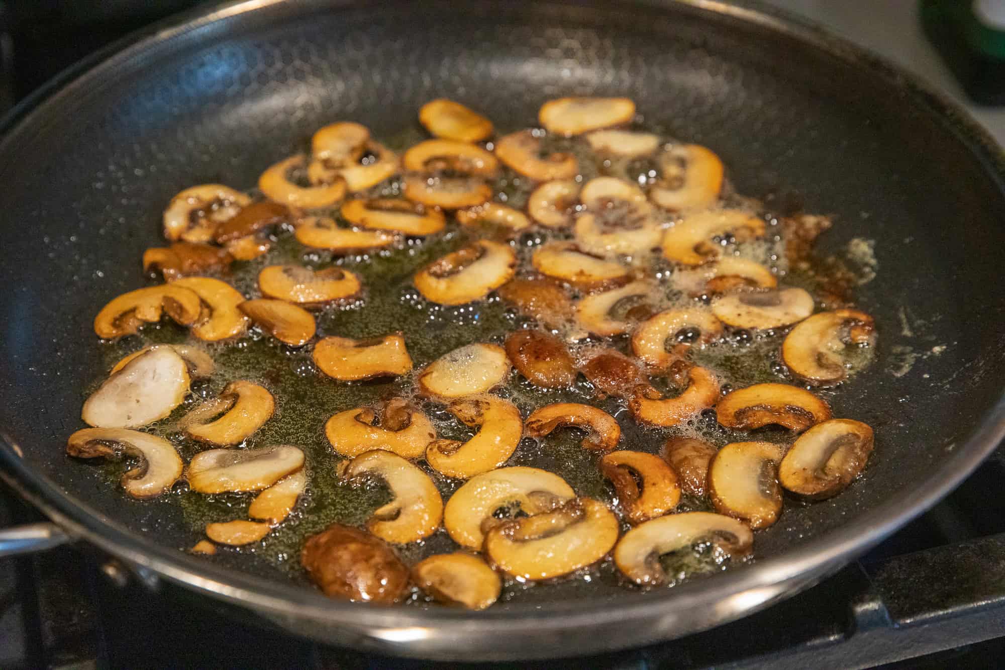Sautéed sliced mushrooms cooking in a black skillet with oil.