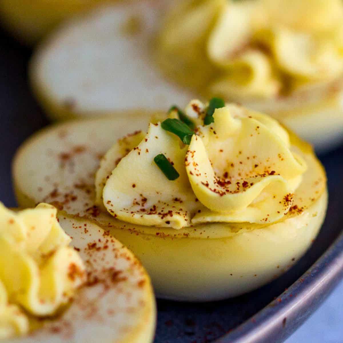 Deviled eggs with creamy filling, garnished with chopped chives and paprika, served on a dark plate.