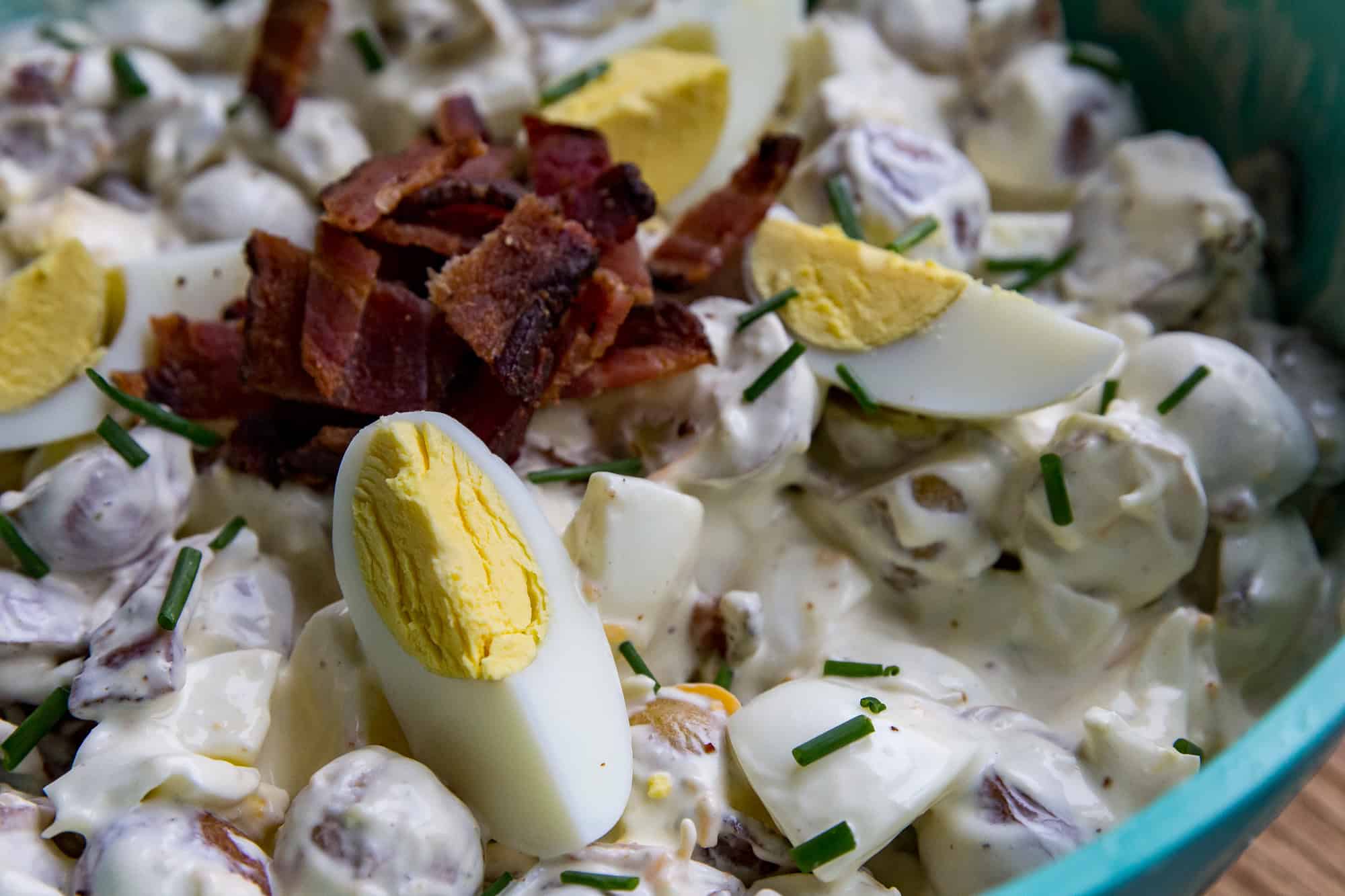 Delicious creamy potato salad topped with bacon, chopped eggs, and chives.