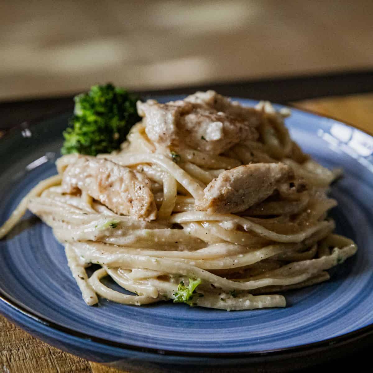 Creamy chicken Alfredo pasta with broccoli on a blue plate.