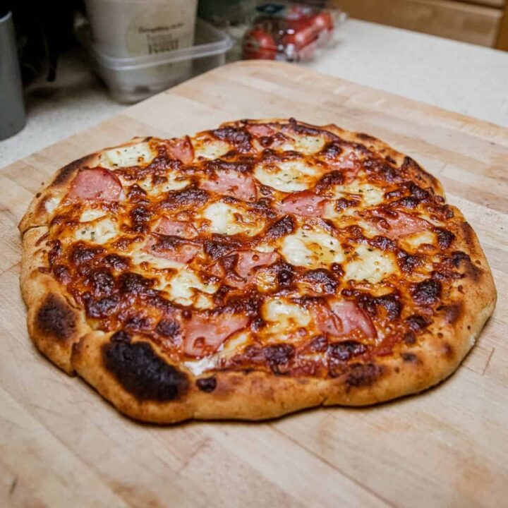 Close-up of a Hawaiian pizza with ham and pineapple on a wooden surface.