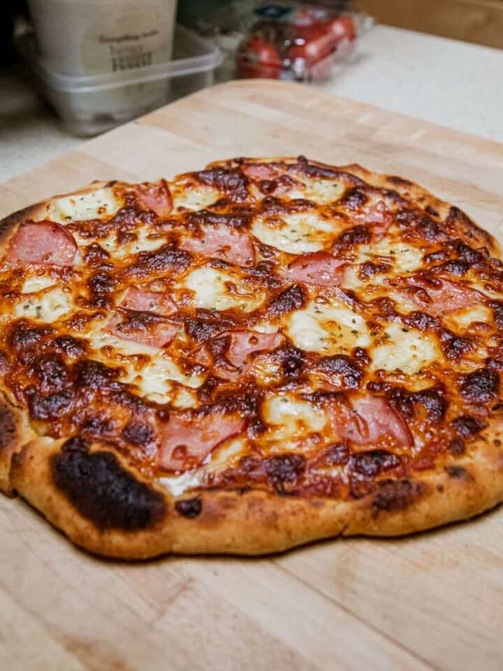Close-up of a Hawaiian pizza with ham and pineapple on a wooden surface.