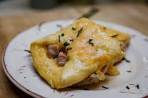 Delicious cheesy ham breakfast casserole with herbs on a white plate.