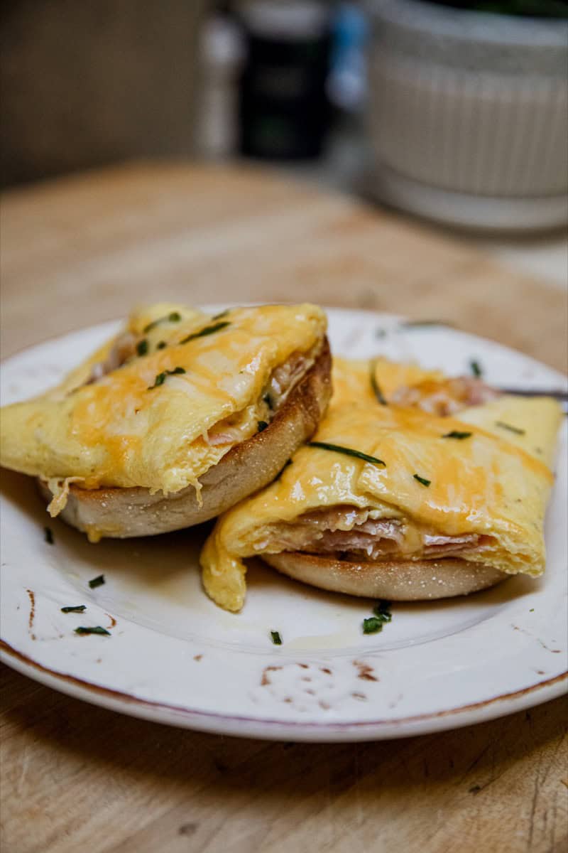 Delicious cheesy ham and cheese omelets served on a white plate, garnished with herbs.