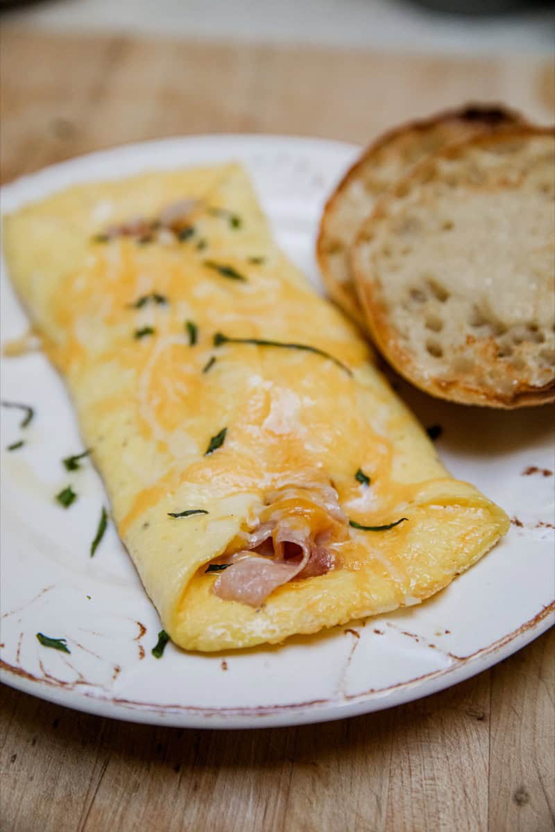 Omelette with ham and herbs served with a slice of rustic bread on a white plate.