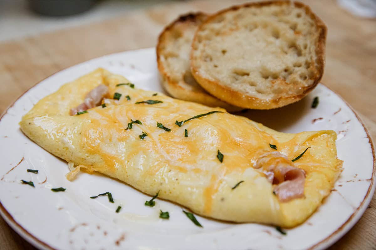 Omelette with ham and cheese served with toasted bread slices on a white plate.