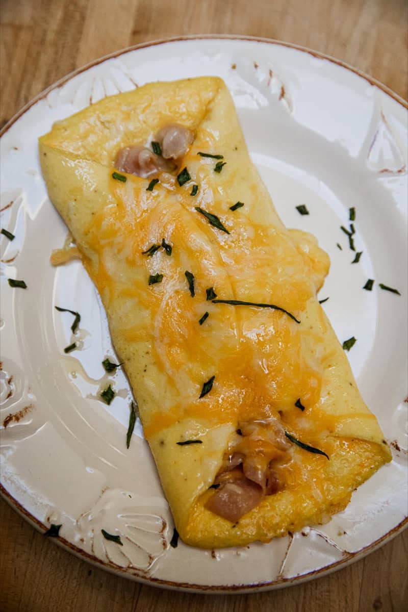 Fluffy ham and cheese omelette garnished with herbs on a white plate.