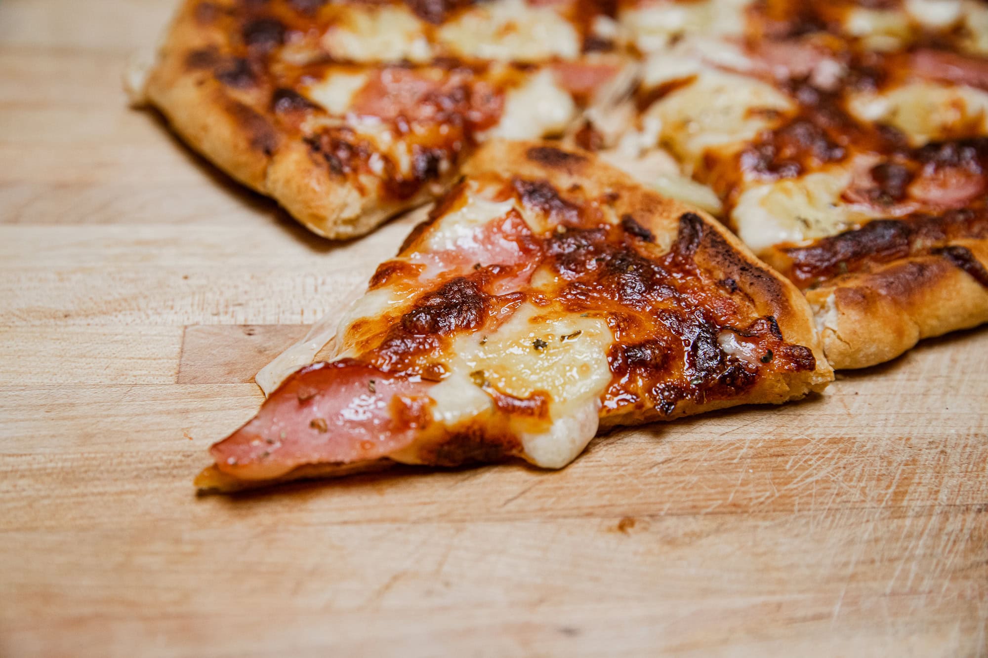 Close-up of a slice of grilled Hawaiian pizza with ham and pineapple.