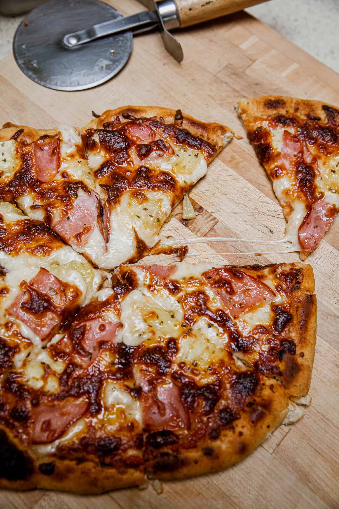 Close-up of a slice of Hawaiian pizza with ham and pineapple on a wooden board.