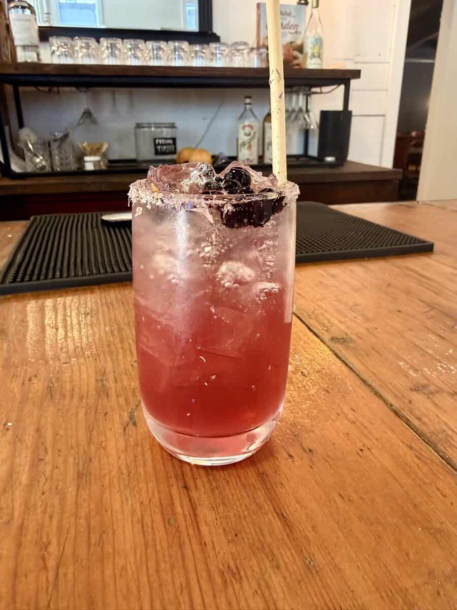 Pink berry cocktail with ice and a straw on a wooden bar.