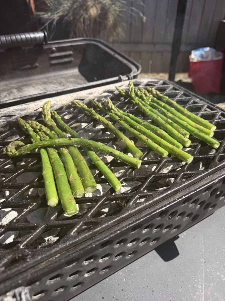 Fresh green asparagus spears grilling on barbecue grill outdoors.
