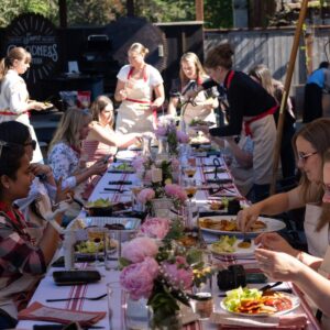 Group of girls and women enjoying outdoor dinner with grilled food and flowers.