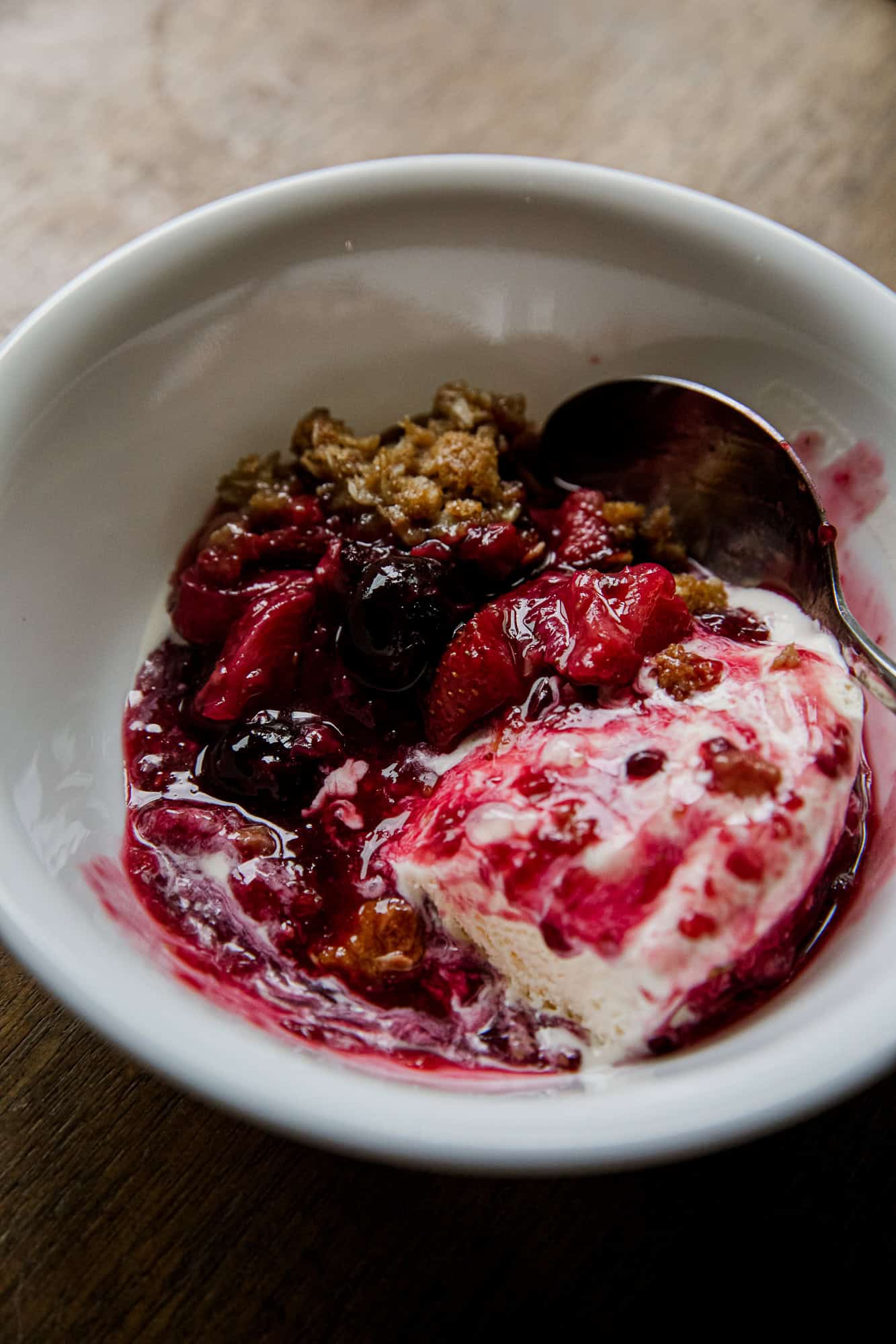 Close-up of berry crisp with ice cream in a white bowl.